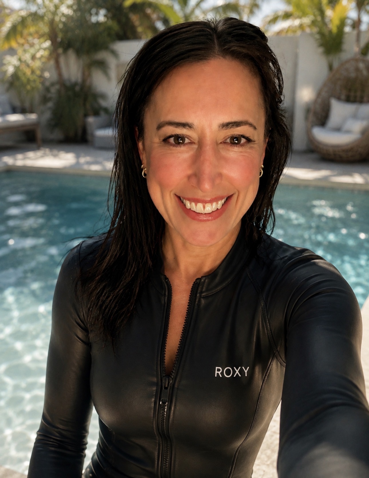 Meredith Sommers smiling in a black wetsuit at the edge of a sunlit pool
